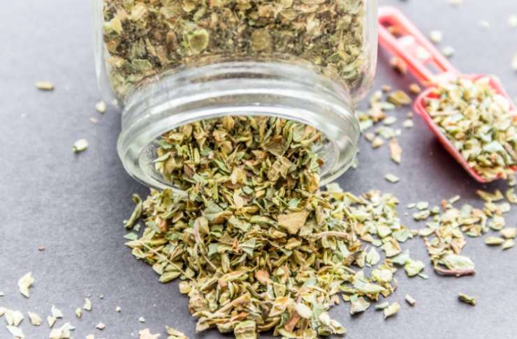 barattolo di origano e accanto un cucchiaino pieno di origano