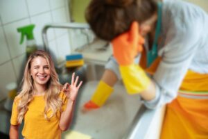 donna scocciata di fronte a lavandino intasato e un'altra sorridente che fa ok con le mani